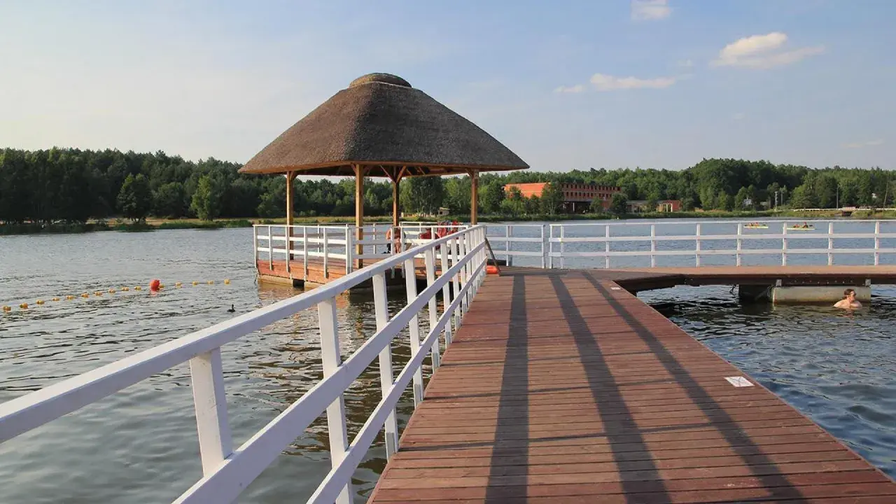 Drewniane molo nad zalewem Siemiatycze, z altaną krytą strzechą. W wodzie kąpie się osoba.