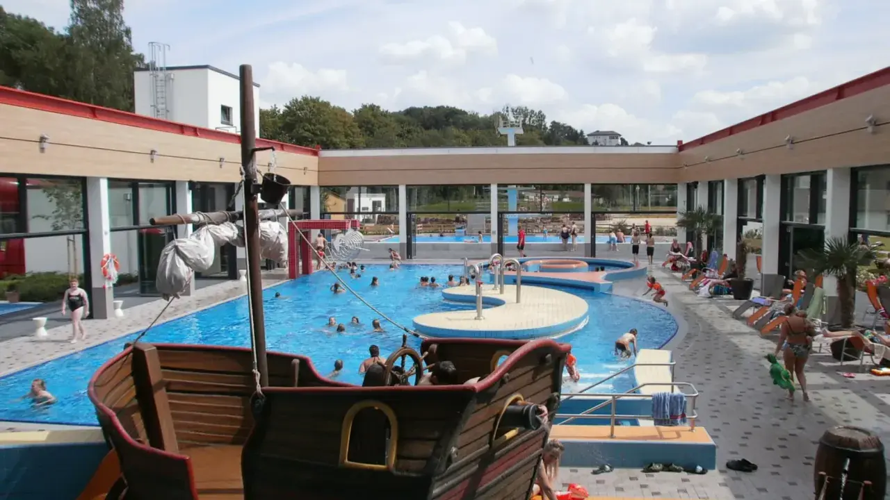 Ein Piratenschiff-Spielplatz in einem Freibad mit vielen Badegästen.
