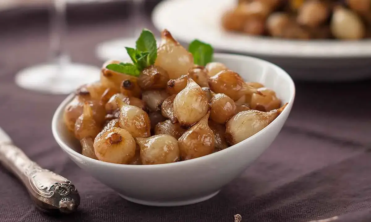Ciotola di cipolle in agrodolce caramellate, guarnite con menta fresca.