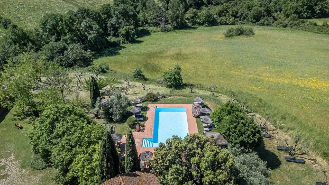 Piscina azzurra circondata da alberi e campi verdi, perfetta per una vacanza in Toscana.
