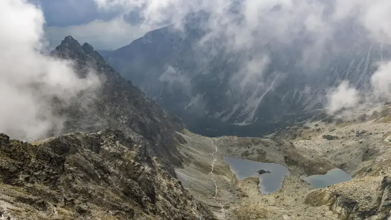 Widok na skaliste zbocza i dwa jeziora w Tatrach, rysy od strony polskiej. Mgła otula szczyty.