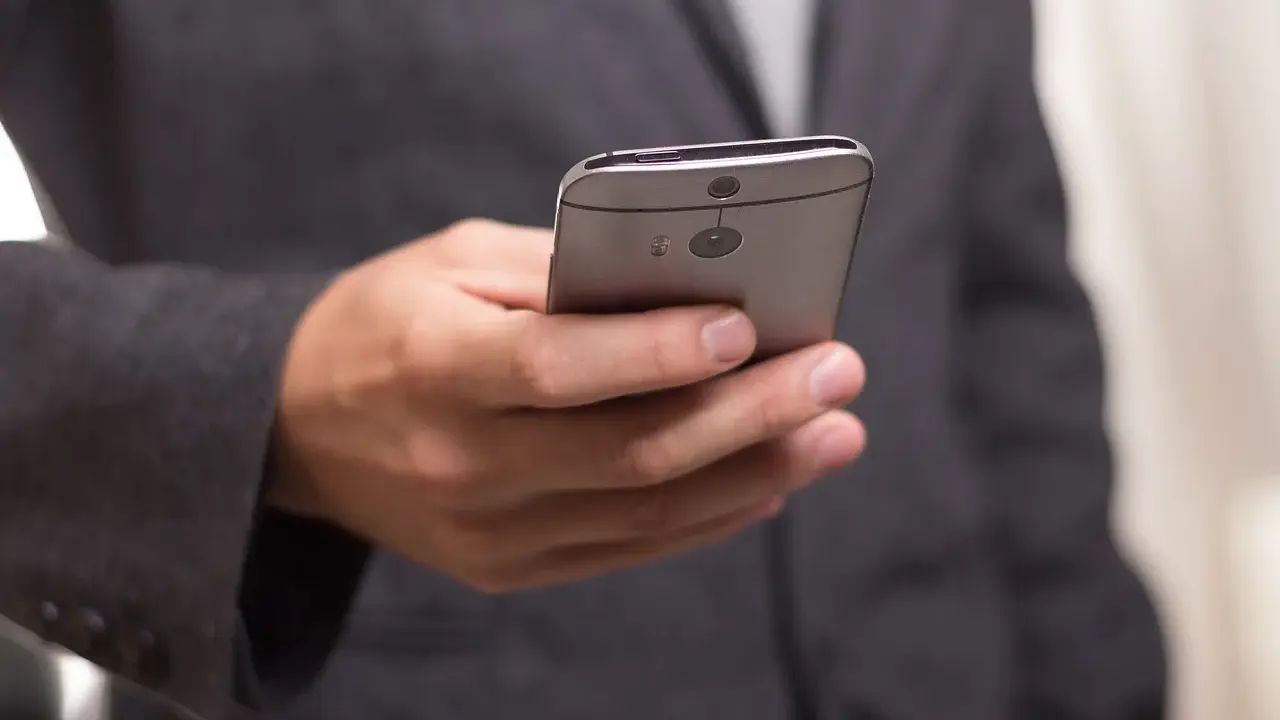Mężczyzna w garniturze trzyma telefon, być może otrzymuje wiadomość o zawieszeniu działalności.