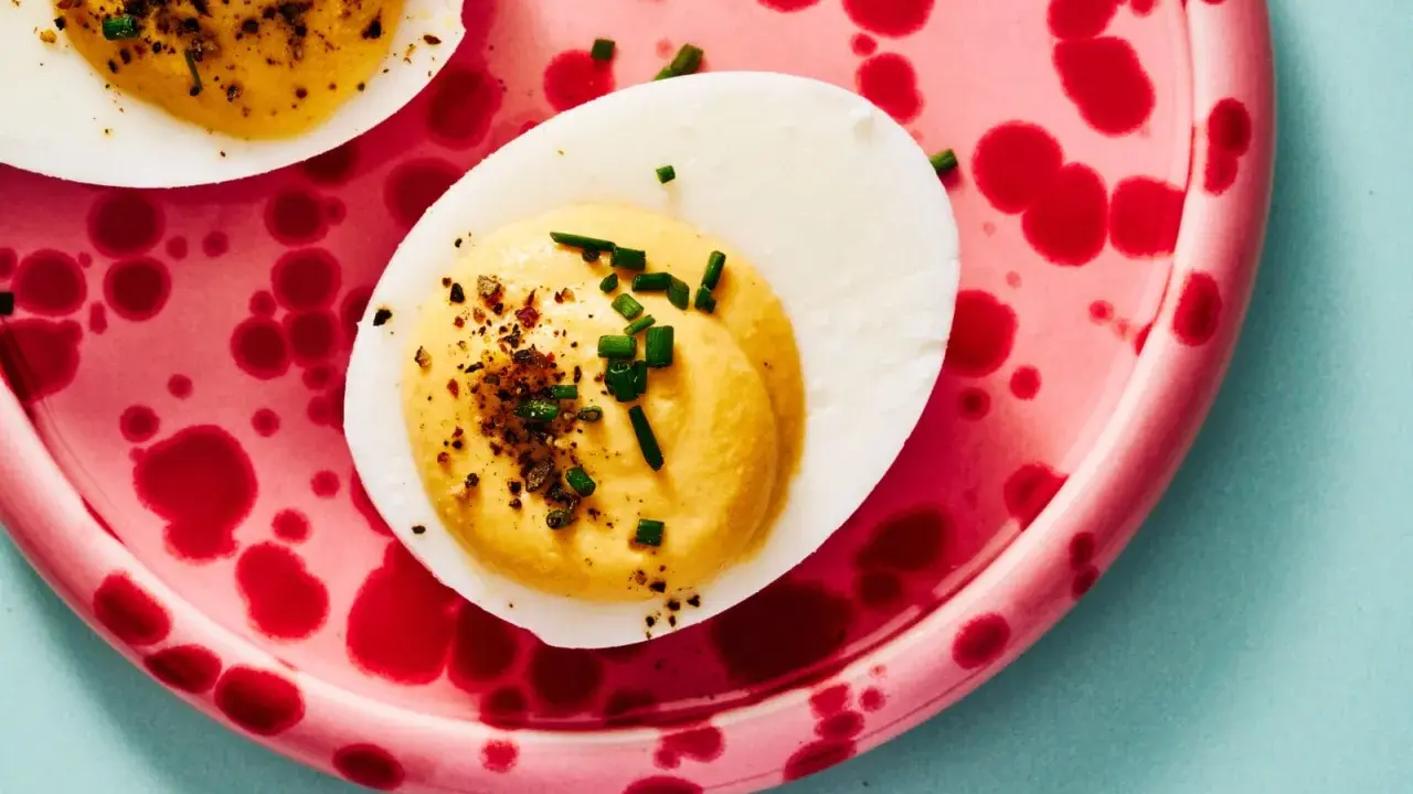 Deviled eggs deutsch: halbe hartgekochte Eier mit cremiger Füllung, bestreut mit Schnittlauch und Gewürzen, auf einem pinkfarbenen Teller mit roten Tupfen.