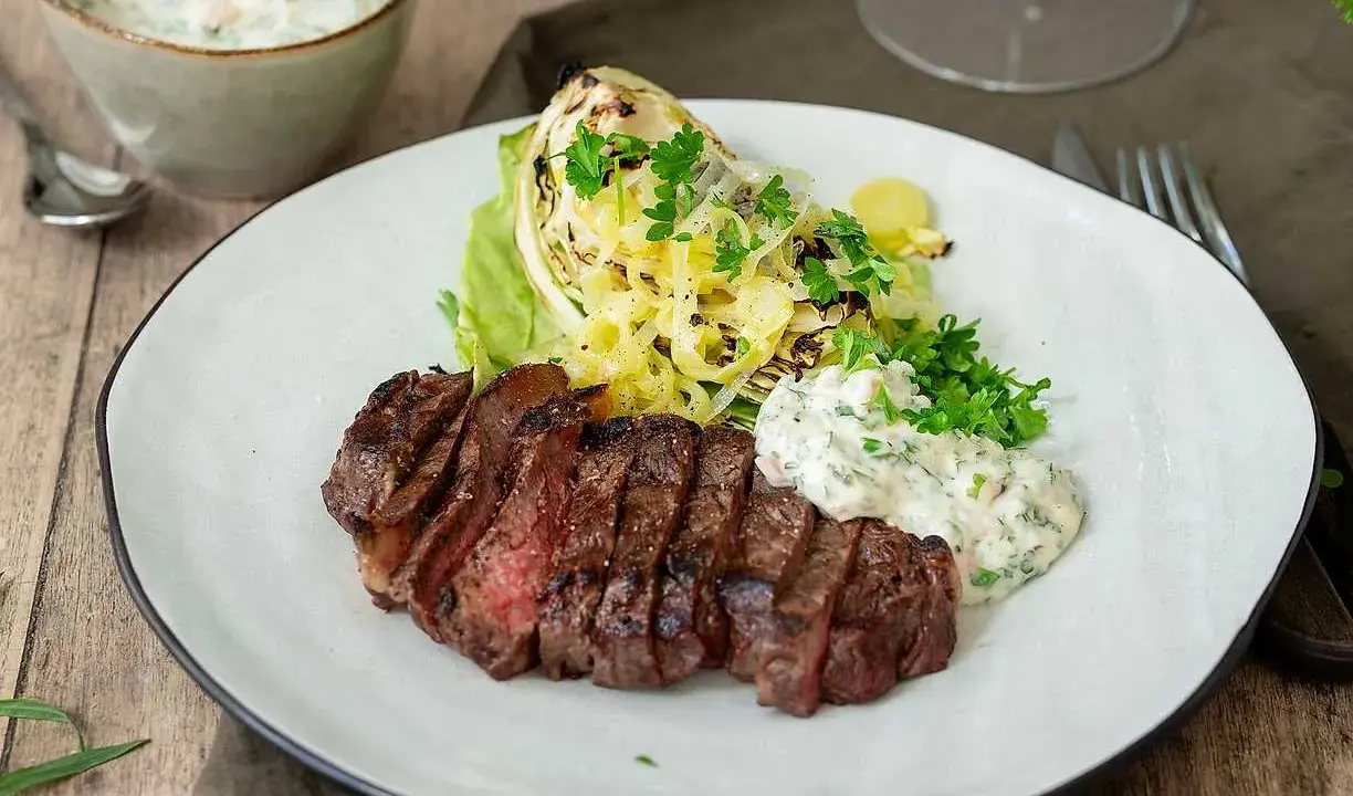 En saftig grillad ryggbiff serveras med krispig sallad, grillad kål och en krämig sås.