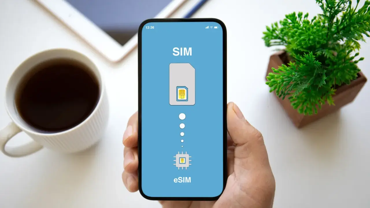 Dłoń trzyma smartfon z ekranem pokazującym proces aktywacji eSIM. Obok kubek kawy i roślinka.