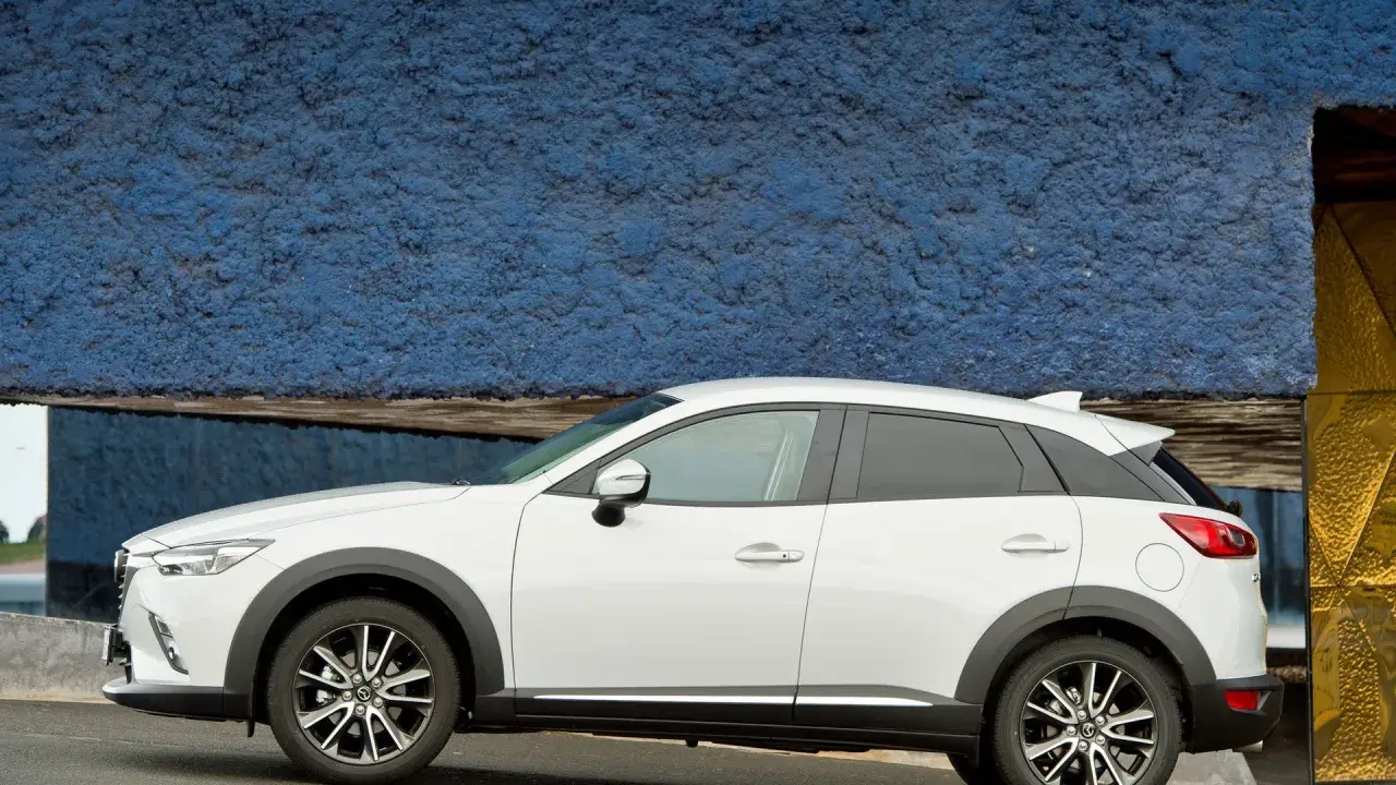 Biała Mazda CX-3 na tle niebieskiej ściany. Sprawdź aktualną mazda cx3 cena i wybierz swój wymarzony samochód.