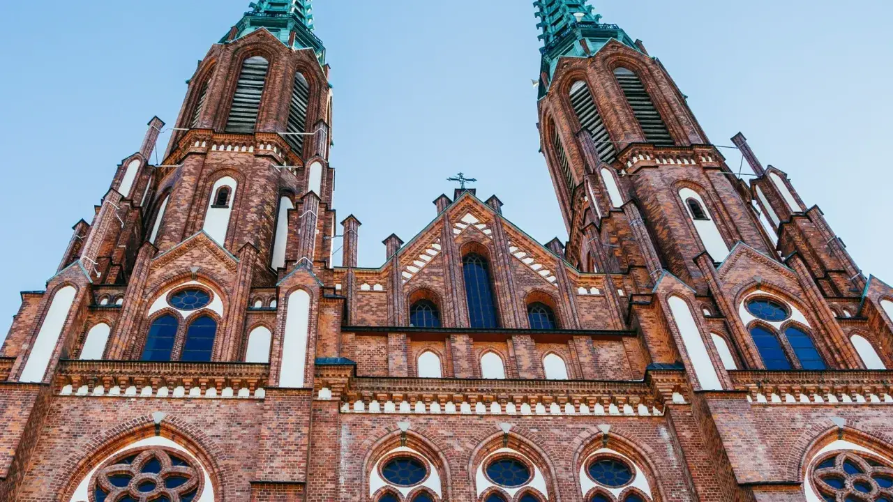 Dwie wieże ceglanego kościoła z zielonymi iglicami, jeden z najpiękniejszych kościołów w Polsce, pod błękitnym niebem.