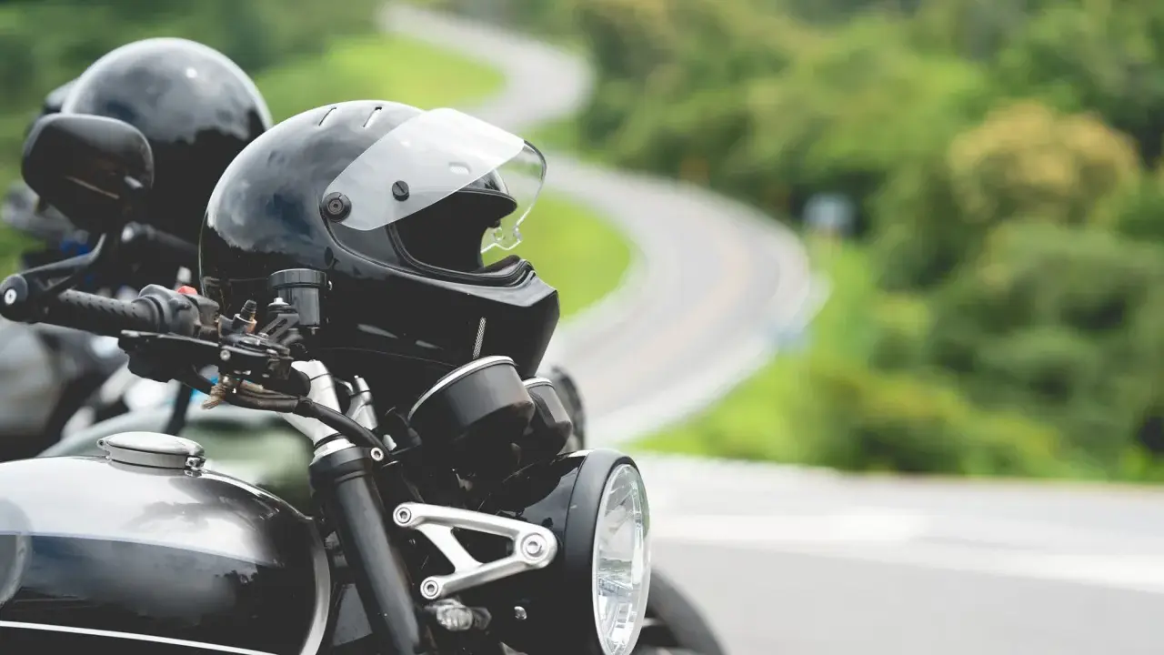 Gotowe na przygodę? Zastanawiasz się nad prawem jazdy na motor i wiekiem? Dwa kaski czekają na motocyklistów na krętej drodze.