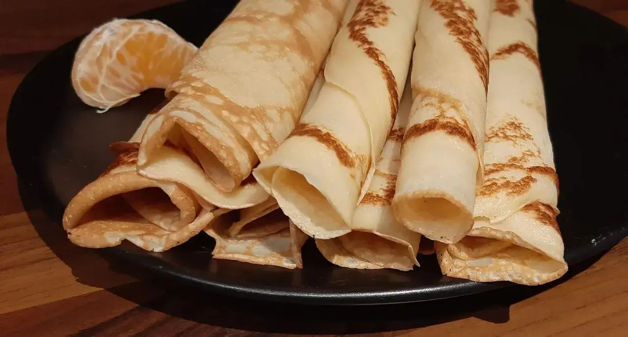 Crêpes à la bière roulées, dorées et légères, servies sur une assiette noire avec un quartier d'orange. Un délice !