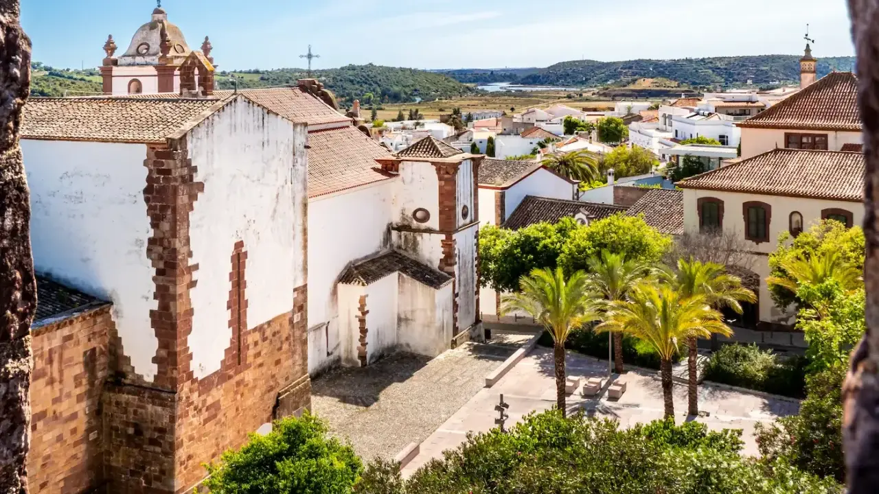 Blick über die weißen Häuser und Palmen von Silves, Portugal, mit einer Kirche im Vordergrund.