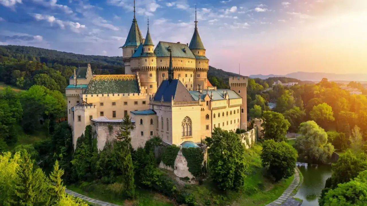 Bajkowy zamek otoczony zielenią, idealne miejsce na nocleg w zamku. Słońce zachodzi nad wzgórzami, tworząc magiczną atmosferę.