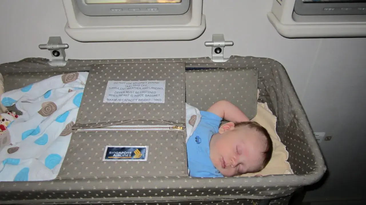 Śpiące dziecko w wózku dla dziecka Singapore Airlines podczas lotu. Wygodny enter air wózek dla dziecka zapewnia spokojny sen maluchowi.