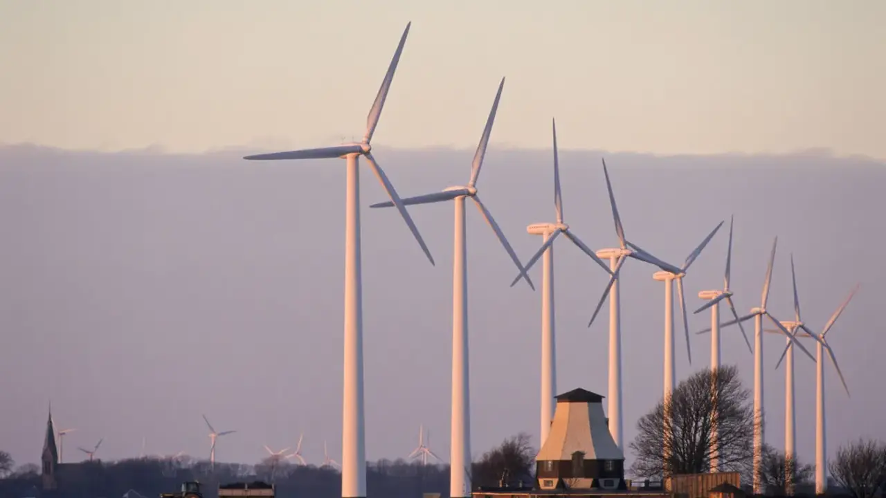 Windräder im Abendlicht, ein Traktor mit Anhänger und ein alter Mühlenbau symbolisieren die Direktvermarktung von Windstrom in ländlicher Idylle.