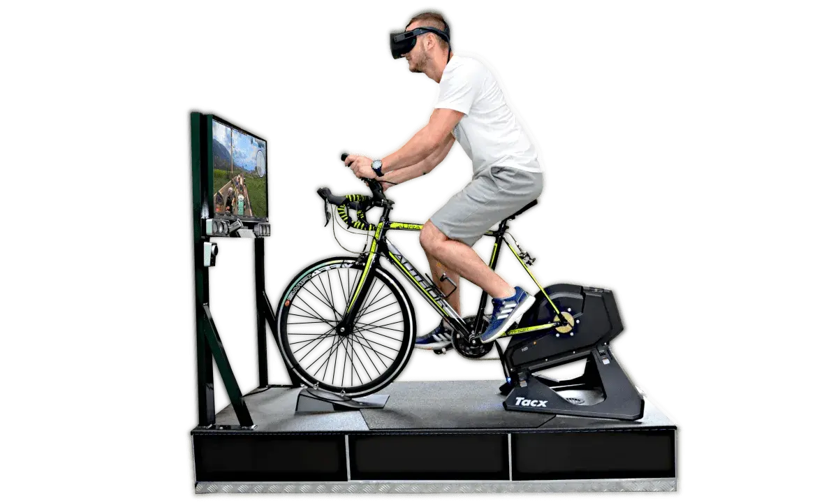 Mężczyzna w goglach VR pedałuje na rowerze stacjonarnym, doświadczając wirtualnej przejażdżki. To zaawansowany symulator jazdy rowerem.
