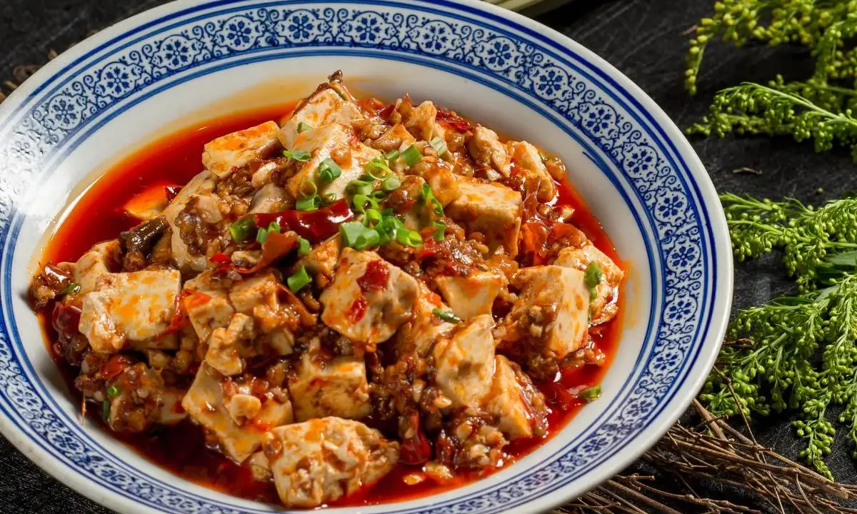 Pikantne tofu w sosie chili, klasyka kuchni syczuańskiej. Danie wygląda apetycznie, ozdobione szczypiorkiem.
