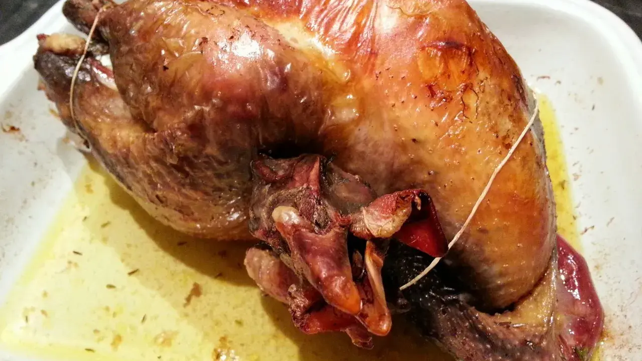 Une pintade au four, dorée et juteuse, repose dans un plat blanc, baignant dans son jus savoureux.