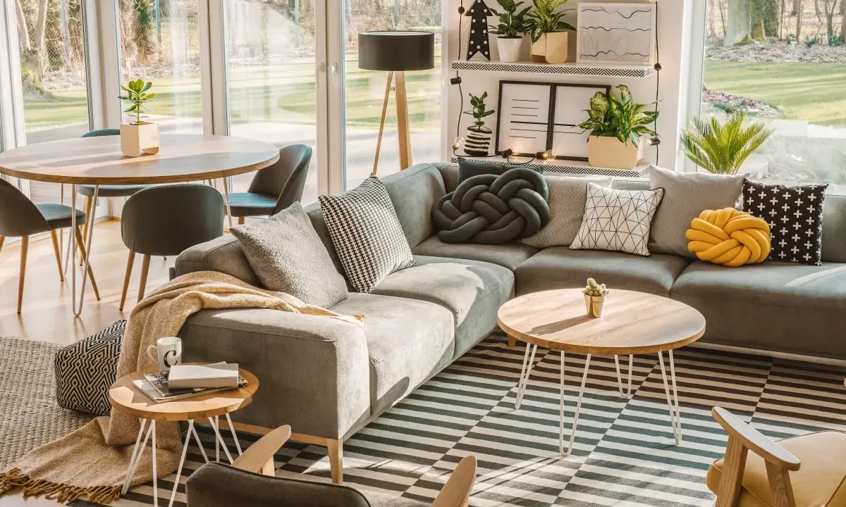Un salón moderno y acogedor con sofá gris, alfombra de rayas, mesa de centro de madera y grandes ventanales que dejan entrar la luz natural.