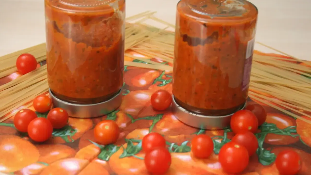 Zwei Schraubgläser mit selbstgemachter Tomatensauce, umgeben von frischen Tomaten und Spaghetti. Perfekt zum Tomatensauce einkochen.