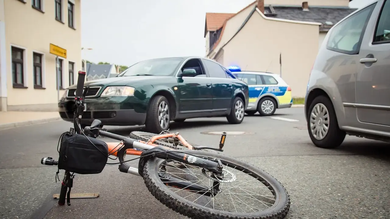 Wypadek drogowy: przewrócony rower, samochód i radiowóz policyjny. Maksymalne obciążenie roweru mogło przyczynić się do zdarzenia.