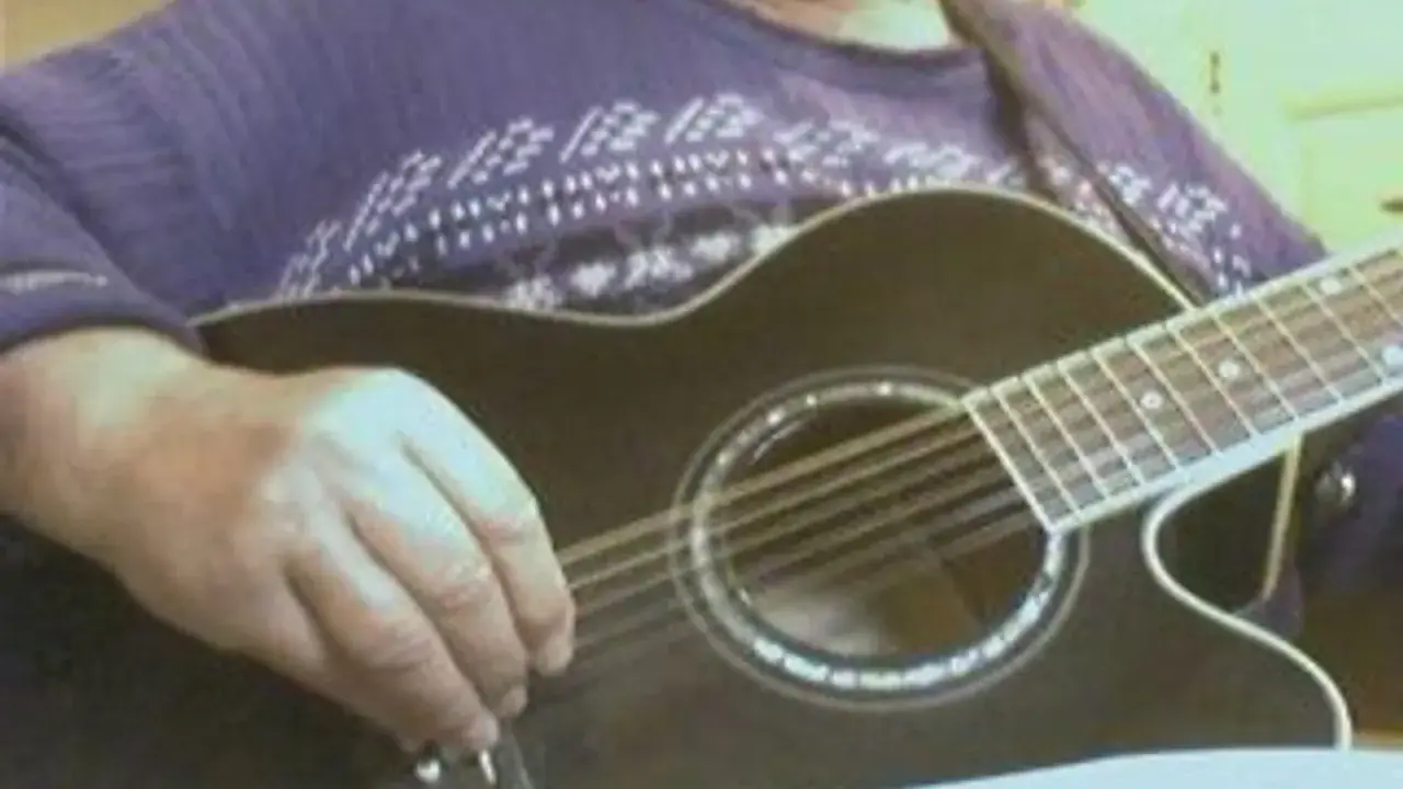 Main d'un musicien ajustant l'accordage 12 cordes d'une guitare acoustique noire.