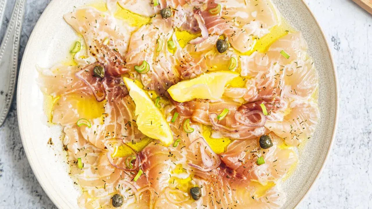 Délicieux carpaccio de saumon, fines tranches de poisson cru arrosées d'huile d'olive, garnies de câpres, oignons rouges et quartiers de citron.