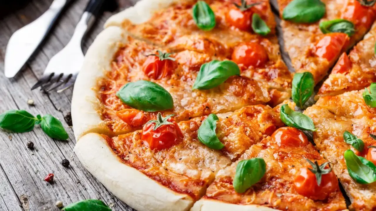 Pyszna pizza Margherita, klasyka włoskiego jedzenia, z pomidorkami koktajlowymi i bazylią na drewnianym blacie.
