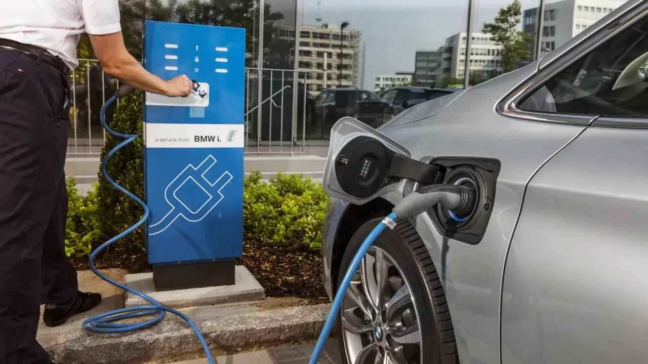 Un uomo collega un'auto elettrica a una colonnina di ricarica BMW i. Un passo verso il calcolo risparmio auto elettrica.