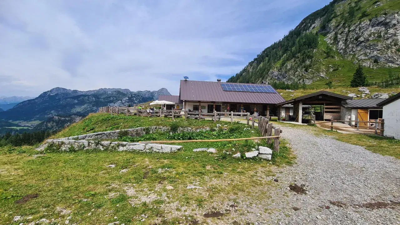 Malga Tuglia, un rifugio alpino con pannelli solari, immerso nel verde con montagne sullo sfondo.