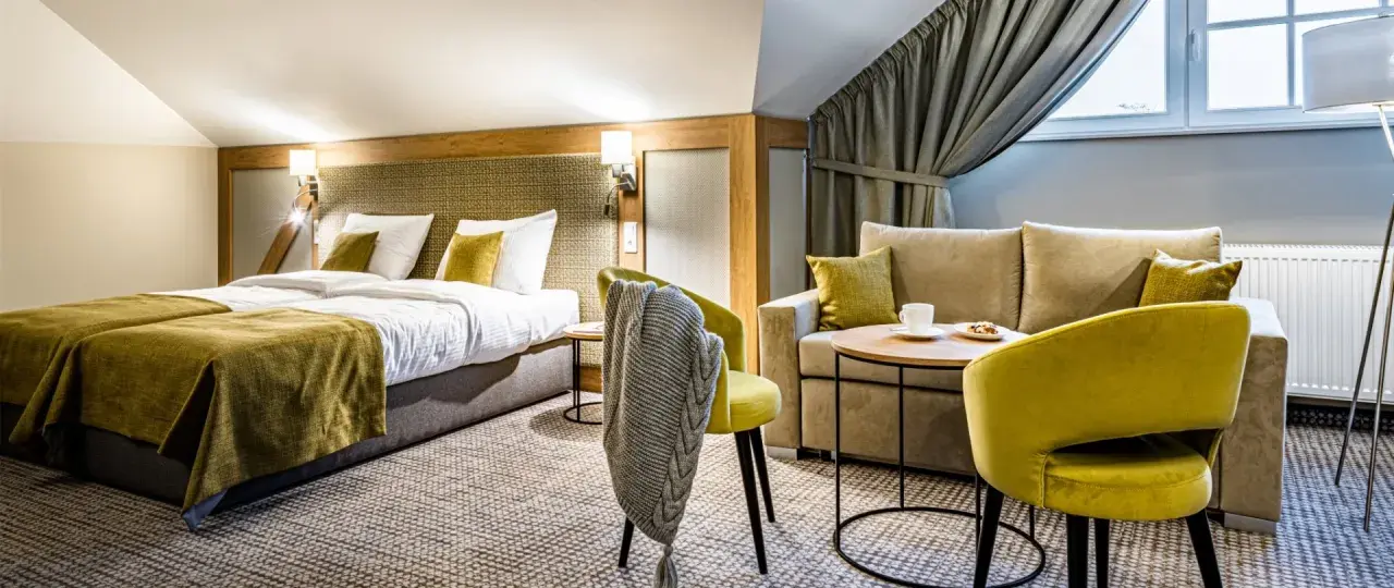 Przytulny pokój hotelowy z dwoma łóżkami, kanapą i fotelami. Idealne miejsce na relaks po podróży.