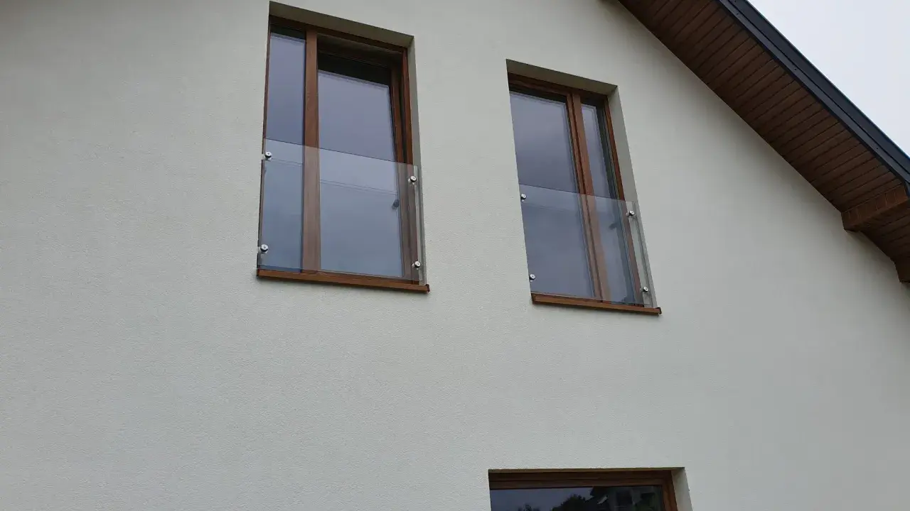 Nowoczesny portfenetr z drewnianymi ramami i szklaną balustradą na białej elewacji.