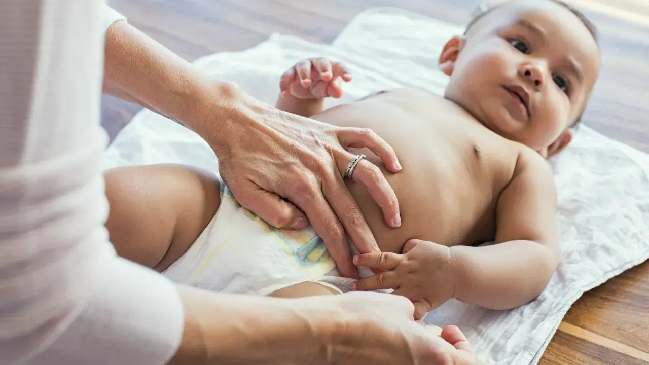 Rąk opiekuna zmienia pieluszkę niemowlęciu. Czy to powód, dlaczego 2 miesięczne dziecko nie sika w nocy?