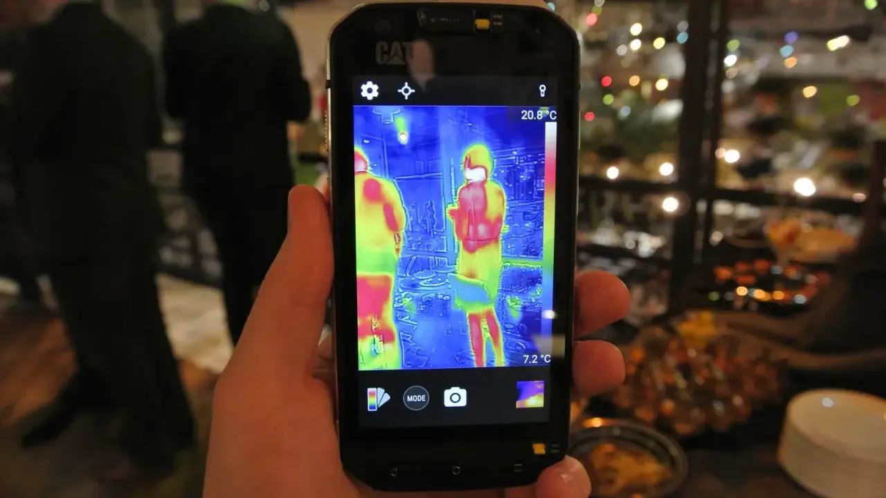 Ręka trzyma smartfon Cat S60 z włączoną termowizją, pokazującą dwie osoby w cieplejszych barwach.