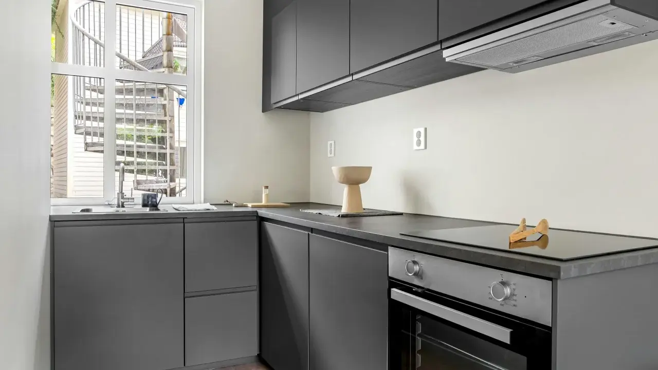 Diseño cocina restaurante moderno con gabinetes grises, encimera oscura y ventana con escalera exterior.