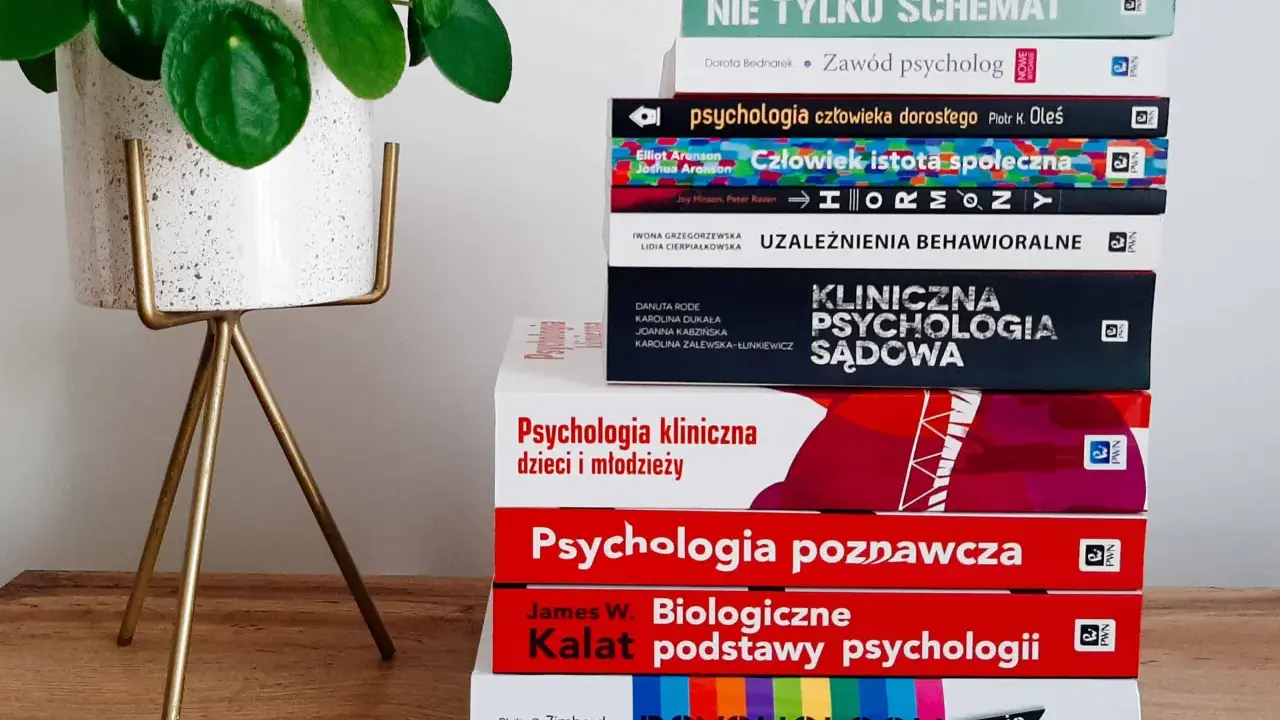Książki o psychologii, w tym "Biologiczne podstawy psychologii" Kalata, na drewnianym tle obok rośliny.