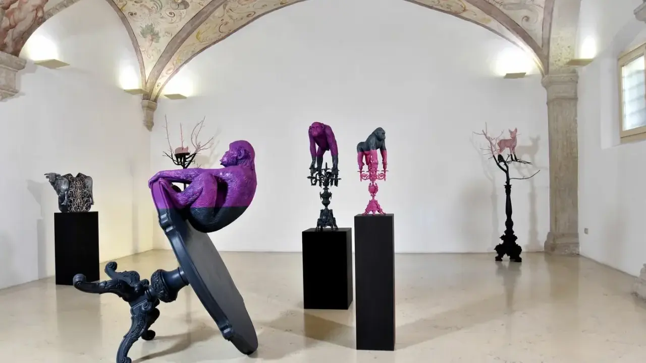 Sculture di scimmie e cervi colorati, opere di **artisti contemporanei famosi**, in una galleria con affreschi sul soffitto.