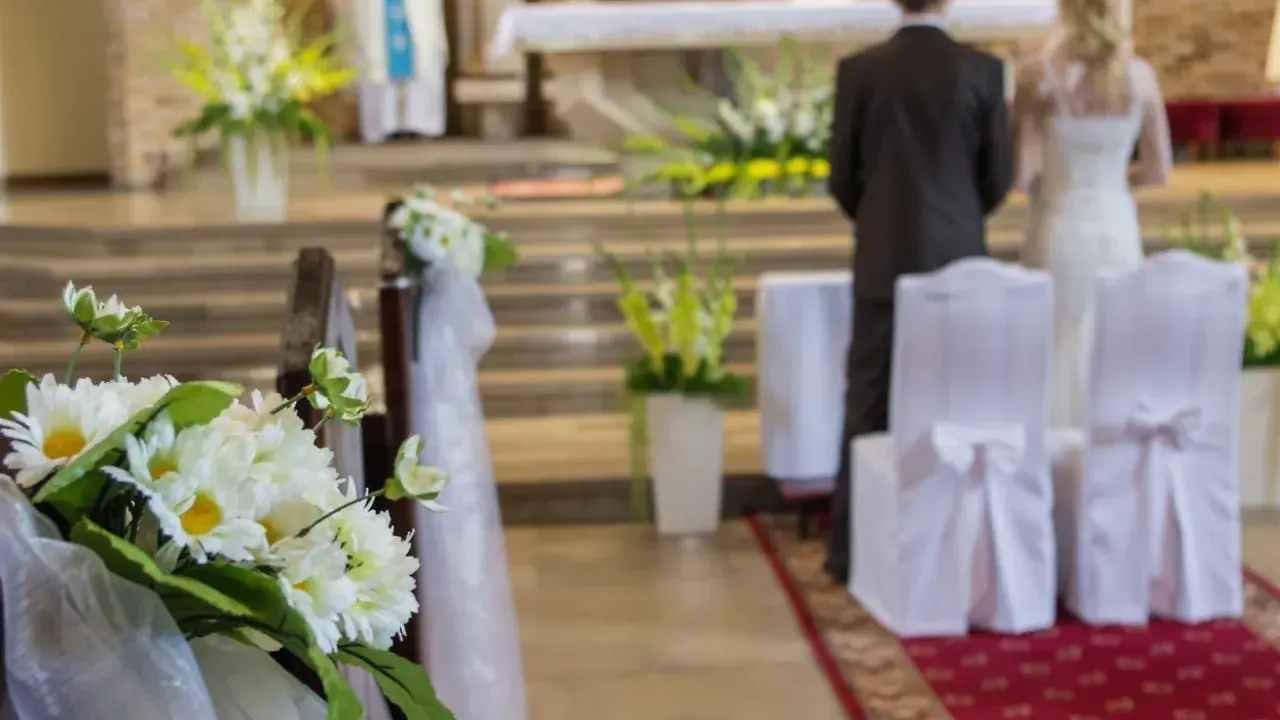Kwiaty zdobią kościelną nawę. Para młoda stoi przy ołtarzu, przygotowując się do ślubu kościelnego jednostronnego.