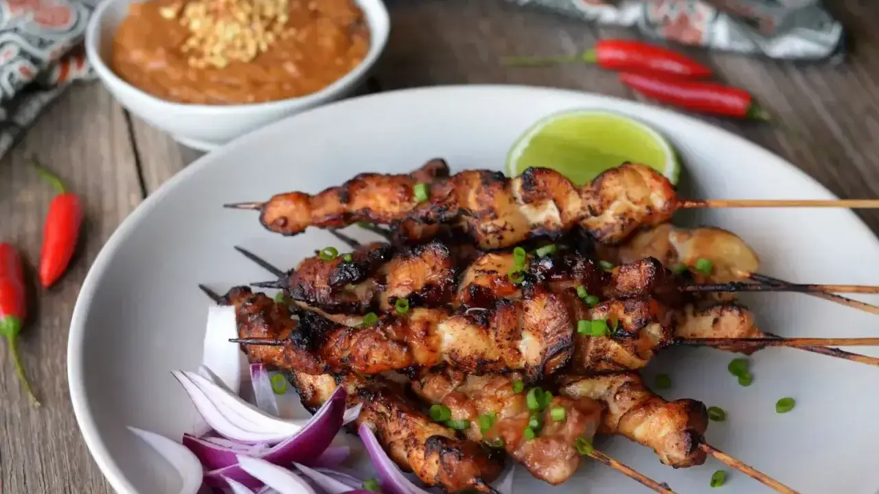 Pyszne satay z kurczaka na patyczkach, podane z sosem orzechowym, limonką i papryczkami chili.
