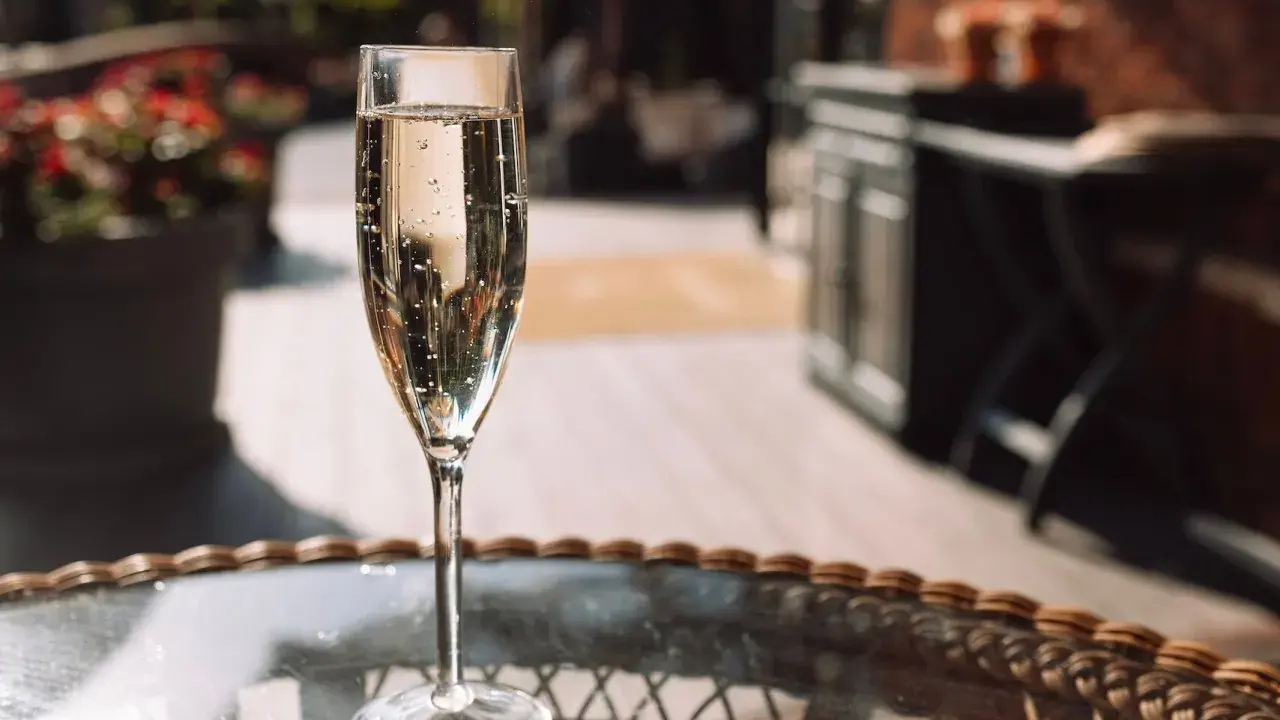 Ein Glas Sekt auf einem Tisch im Freien. Die Bläschen im Glas zeigen, dass der Sekt frisch ist und die Haltbarkeit noch gut ist.