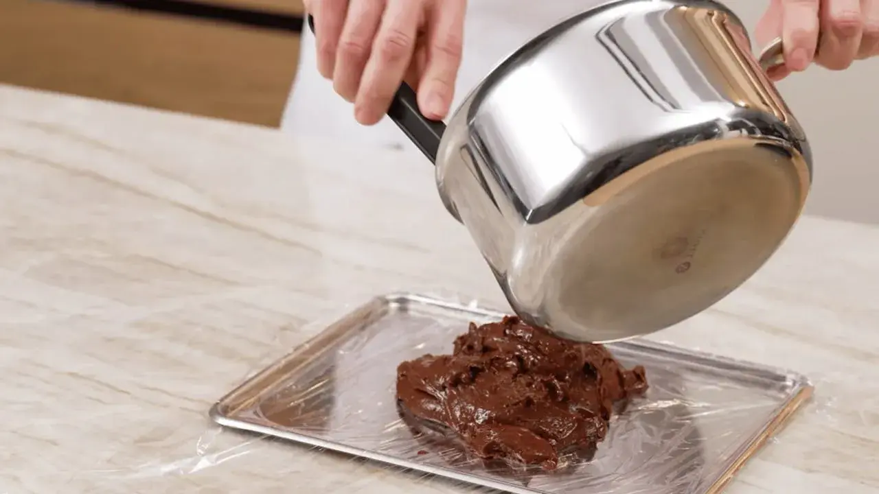 Comment faire fondre du chocolat : une casserole verse du chocolat fondu sur une plaque recouverte de film plastique.