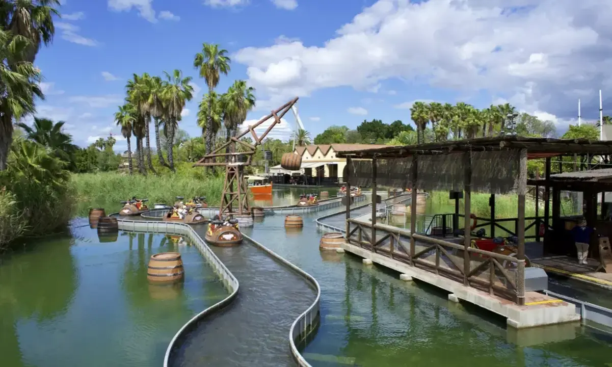 Atracción acuática con barcas y barriles flotantes, ideal para saber donde ir de vacaciones con niños. Palmeras y cielo azul.