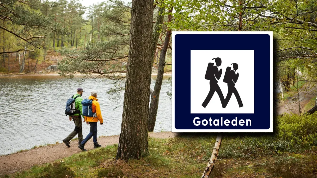 Två vandrare följer en stig vid en sjö, med en skylt för Gotaleden etapper.