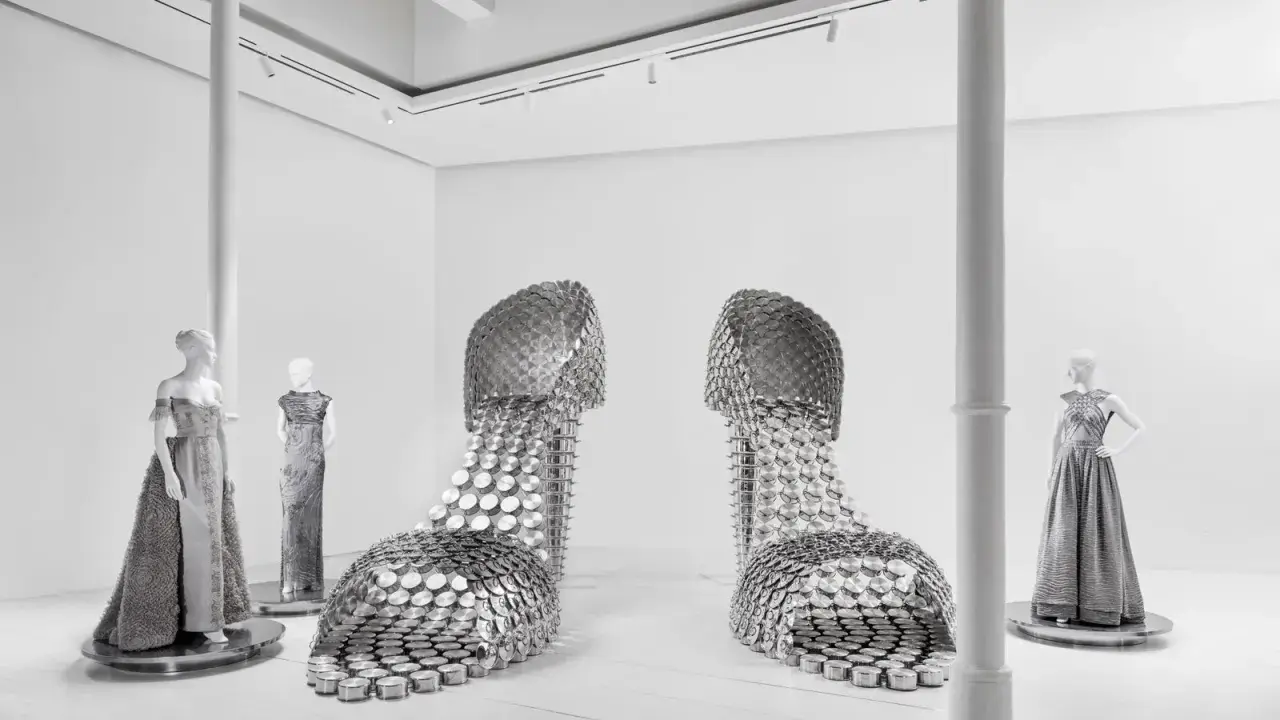 Installazione artistica mostra valentino roma: due enormi scarpe metalliche e abiti da sera su manichini.