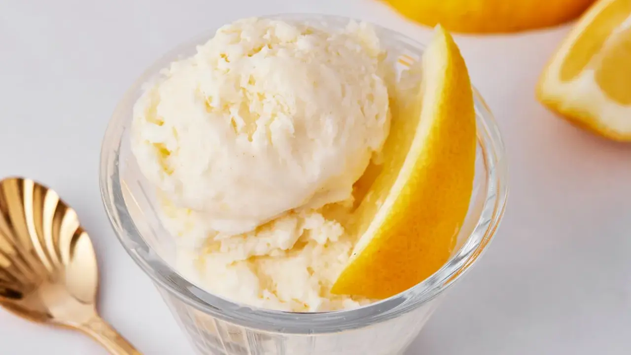 Erfrischendes zitroneneis selber machen: cremiges Eis in einer Glasschale, garniert mit Zitronenspalten und einer goldenen Löffel.