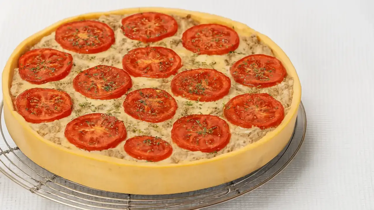 Une délicieuse quiche au thon, garnie de rondelles de tomates fraîches et d'herbes, prête à être dégustée.