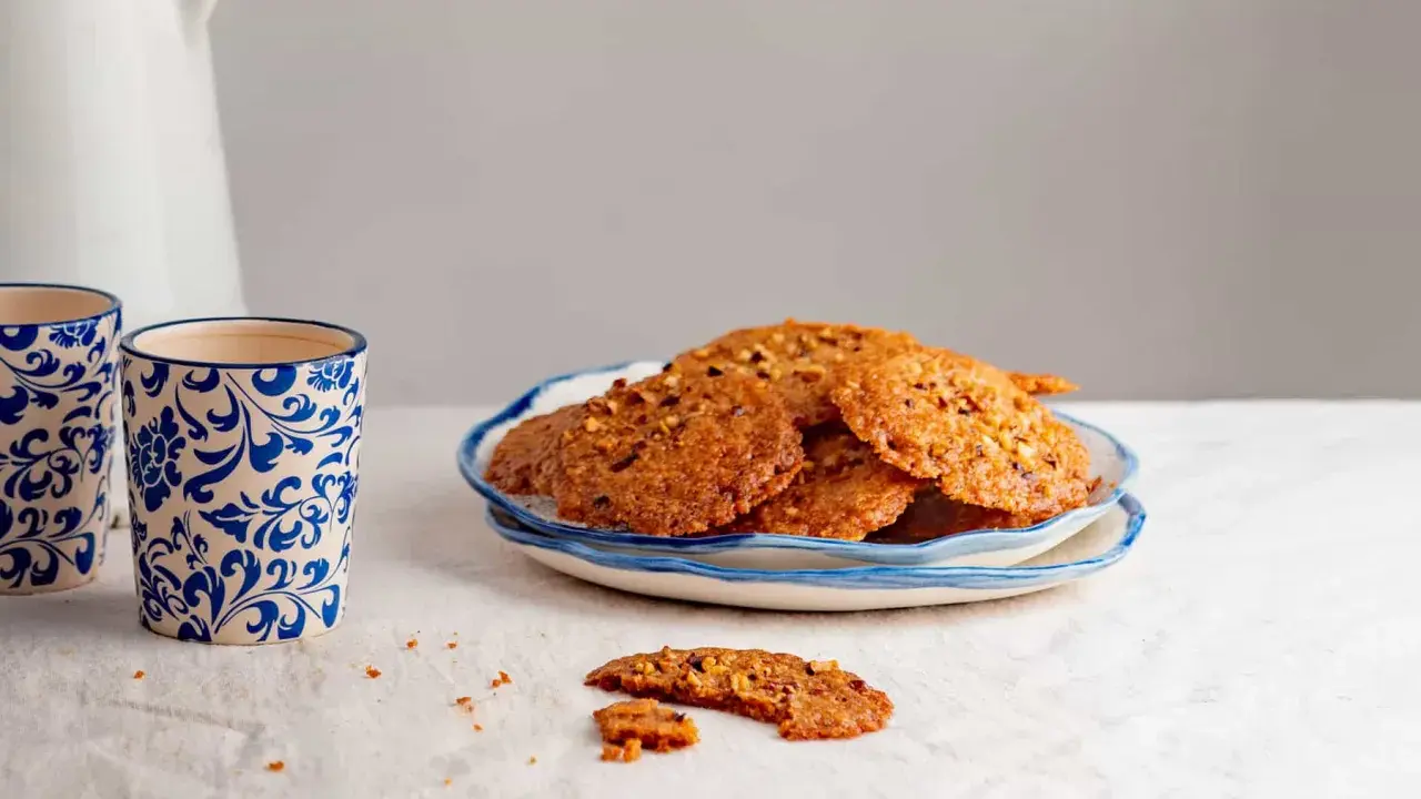 Deliciosas galletas de jengibre con trozos de nuez, servidas en un plato azul y blanco. Perfectas para acompañar un café.