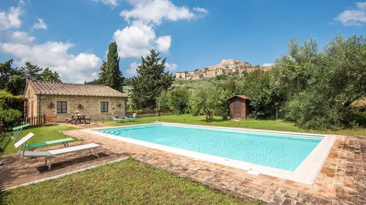 Piscina in un casale in pietra nel Val d'Orcia, Italia, con un borgo medievale sullo sfondo.
