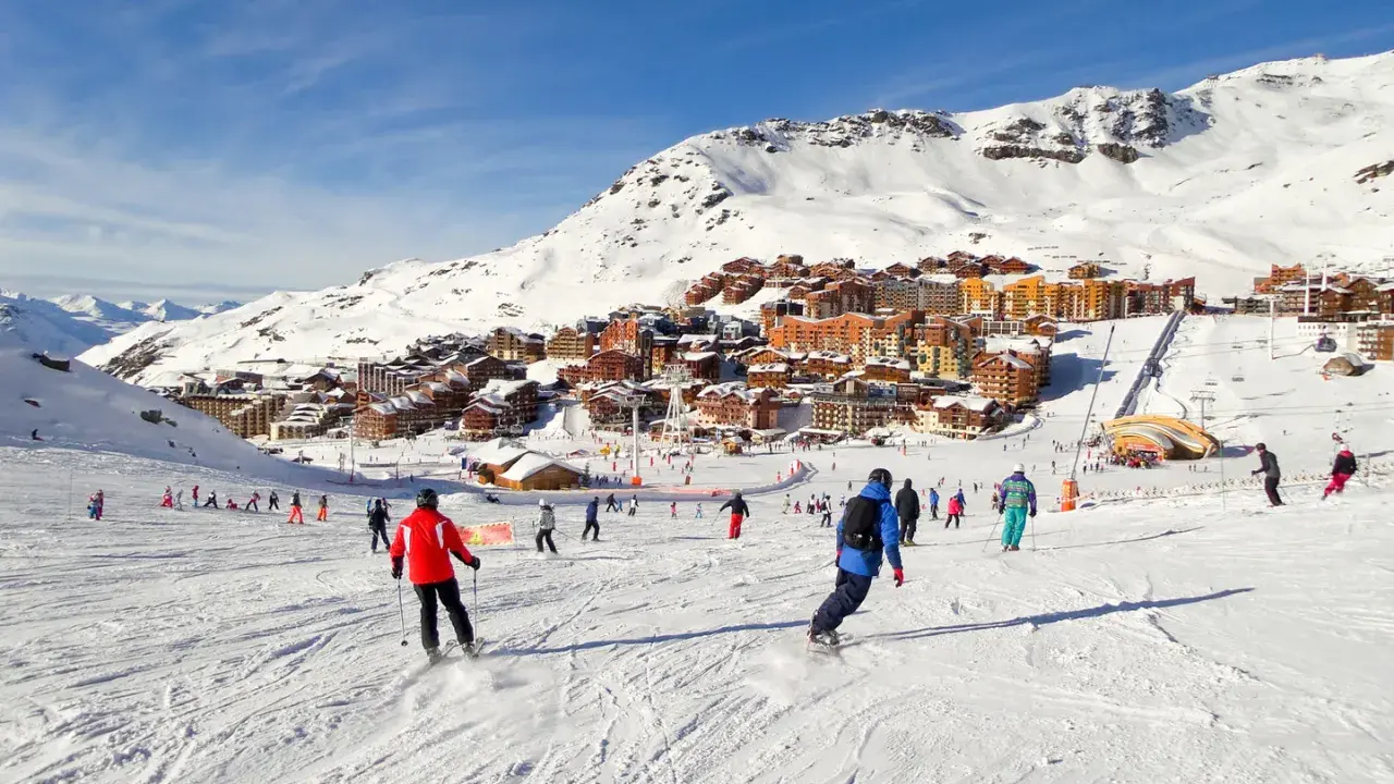 Ośrodek narciarski we francuskich Alpach. Tłumy narciarzy i snowboardzistów na stoku, w tle zabudowania. Francja narty gdzie najlepiej? Tutaj!