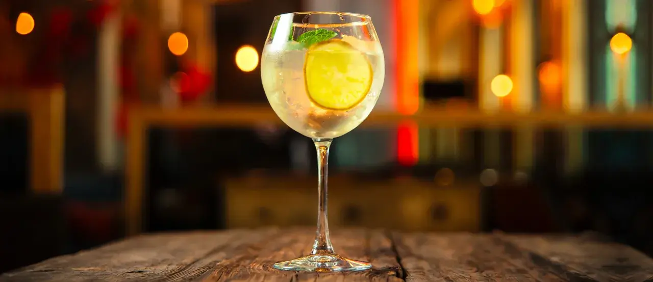 Erfrischender Martini Bianco Spritz mit Zitrone und Minze auf einem Holztisch, im Hintergrund unscharfe Lichter.