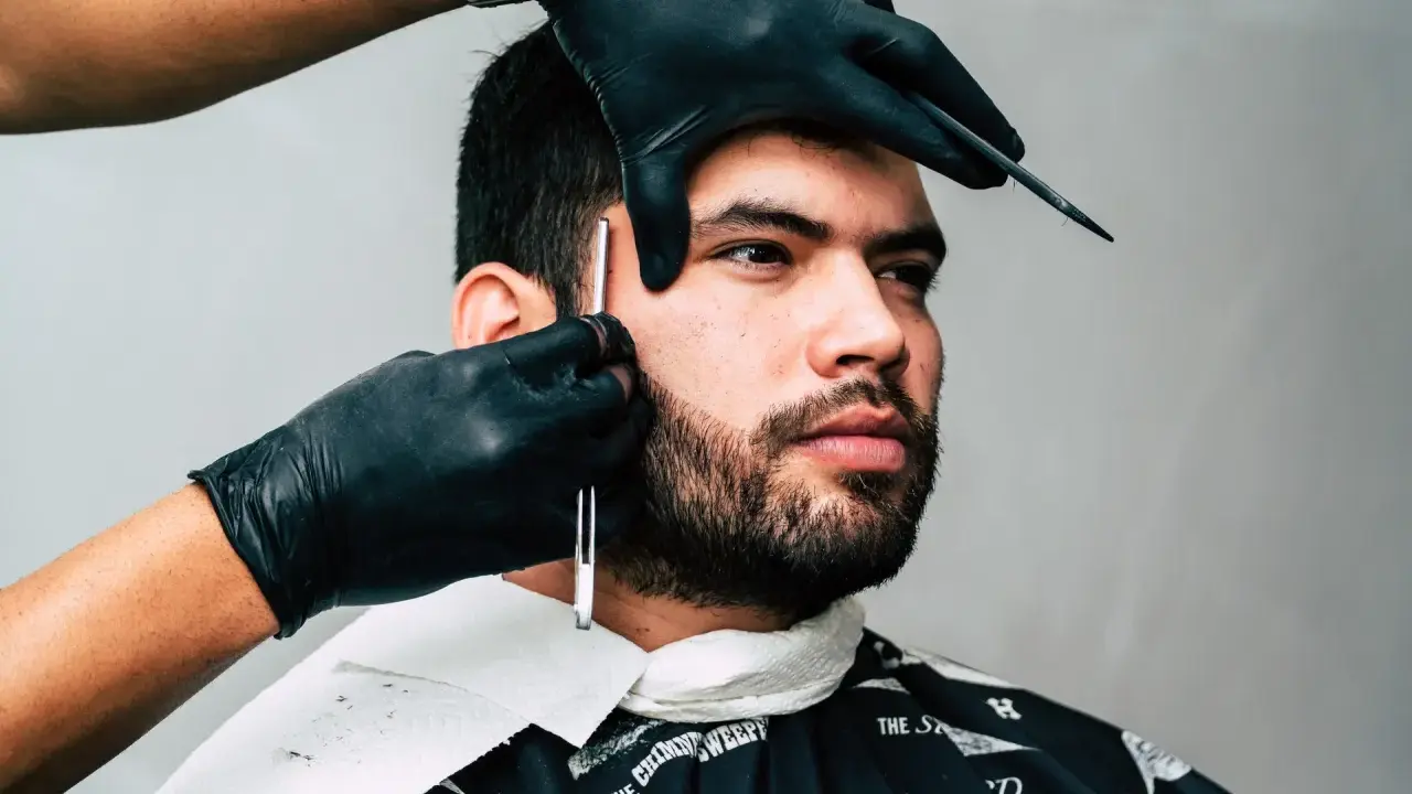 Barber precyzyjnie goli zarost brody ostrym narzędziem.