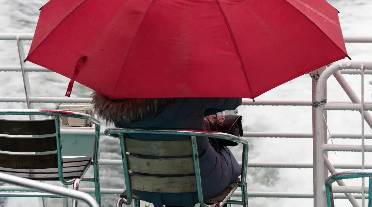 Person under röd paraply på en båt, omgiven av brusande vatten. En typisk bild av bergen regndagar.